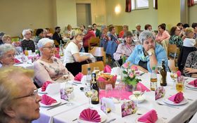 Frauen sitzen im dekorierten Jugendheimsaal und feiern Muttertag