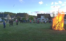 Menschen stehen im Halbkreis in einer Wiese und rechts im Bild brennt ein Pfingstfeuer