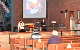 Altarraum der Friedenskirche mit aus Windlichtern gelegtes Kreuz, Pfarrer und Lektorin sitzend, im Hintergrund Leinwand mit Kreuzwegstation