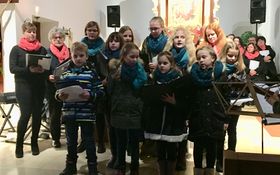 Kinderchor steht in einer Kirche mit der Chorleiterin