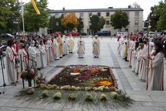 Pfarrer Fenk und Dekan Jeschner stehen vor einem Blumenteppich, als Spalier stehen Ministranten und weitere Priester
