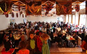 Bunt geschmückter Saal, voll mit Kindern und Erwachsenen, die kostümiert sind