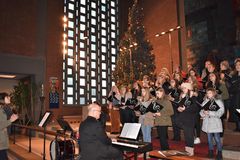 Chor stehend im Altarraum mit Liedermappe in der Hand, im Vordergrund ein Mann am Piano.