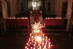 Eine Vielzahl brennender Kerzen auf roten Tüchern, als Kreuzform gelegt. Im Hintergrund steht ein holzkreuz