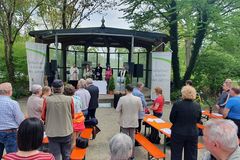 Katholische und evangelische Priester in einem Pavillon, davor stehen Leute an Biergarnituren