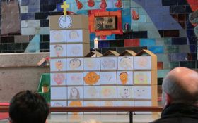 eine Kirche aus Kartons gestapelt, auf den Kartons sind selbst gemalte Kinderportraits