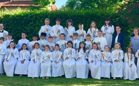 28 Kinder in weißen Gewändern mit kerze in der Hand. Ein Priester im Priestergewand und zwei erwachsene Frauen