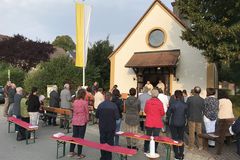 Menschen stehend vor der Michaelskapelle, im Hintergrund eine gelb-weiße Fahne