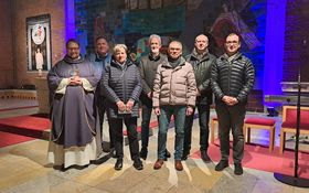 3 Frauen und 7 Männer stehen vor einer Wand, an der ein Holzkreuz hängt