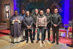 3 Frauen und 7 Männer stehen vor einer Wand, an der ein Holzkreuz hängt