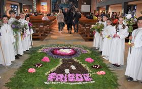 Kommunionkinder stehen neben einem Blumenteppich