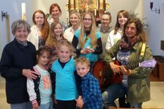 Gruppenfoto mit 10 Kindern und links und rechts je eine erwachsene Frau im Altarraum einer Kirche. Rechte Frau mit umgehngter Gitarre
