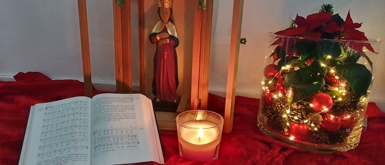 geöffnete Laterne mit der schwangeren Maria, davor brennt eine Kerze und liegt ein Gotteslob