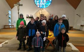 Kinder stehen in einem Altarraum um eine mit Papiersternen gefüllte Krippe