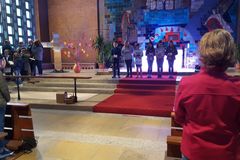 6 Kinder stehen nebeneinander vor einem Altar im Hintergrund ein Kinderchor, ein Kreuz und ein Strauch