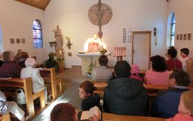 Gläubige sitzen in einer Kapelle und hören einem Pfarrer beim Predigen zu