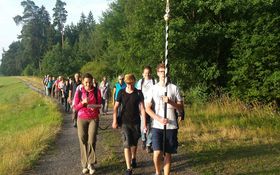 Eine Gruppe Menschen am Waldrand, vorne ein Teenager, der ein Kreuz trägt