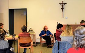 Viele Leute sitzen um Tischen und hören zu, wie aus der Bibel vorgelesen wird.