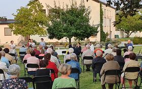sitzende Leute auf einer grünen Wiese, vorne ein katholischer Priester und eine evangelische Lektorin