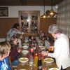 Ein langer Holztisch ist mit weißen Tellern und goldenen Servietten gedeckt. Am Tisch sitzen Kinder und zwei Erwachsene schenken gerade die Getränke ein.