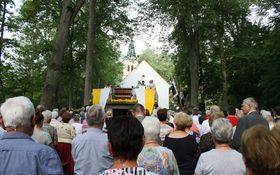 Kirche von Bäumen umringt, Altar, zwei weiß-gelbe Fahnen und viele Menschen von hinten