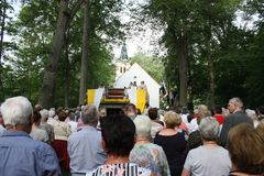 Kirche von Bäumen umringt, Altar, zwei weiß-gelbe Fahnen und viele Menschen von hinten