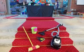 Besen, Eimer, Staubsauger und Lappen liegen auf einem roten Teppich vor dem Altar der Friedenskirche