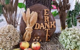 runde Scheibe aus Ton mit dem Wort Erntedank, links und rechts Getreideähren, vorne 3 Äpfel