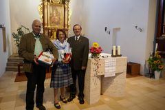zwei Männer und eine Frau in der Mitte mit Geschenken stehen neben einem Altar in der Kirche