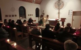 Kapelle mit sitzenden Personen, jeder hat eine Kerze vor sich, der Altarraum ist beleuchtet