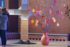 ein Holzkreuz mit Regalen, in denen Boxen stehen, daneben eine Vase mit Zweigen, an denen ausgeschnittene Feuerzungen hängen