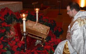 Krippe mit Jesuskind umgeben mit einer Vielzahl von roten Weihnachtssternen, davor kniet Pfarrer Fenk