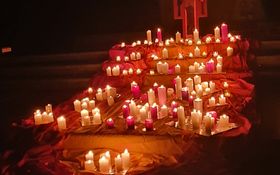 Kerzen läuchten auf rot-gelben-Tüchern vor einem Taizekreuz in der Dunkelheit