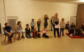 16 Kinder stehen im Halbkreis in einem leeren Raum