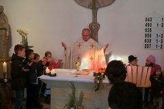Pfarrer mit ausgebreiteten Händen hinterm Altar, link und rechts kinder