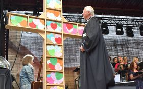 Regalartiges Holzkreuz auf einer Bühne mit bunten Herzen beklebt